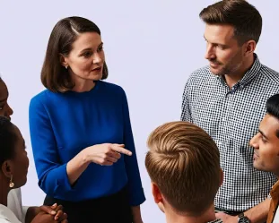 Group of diverse coworkers having a discussion with a woman in blue speaking and pointing.
