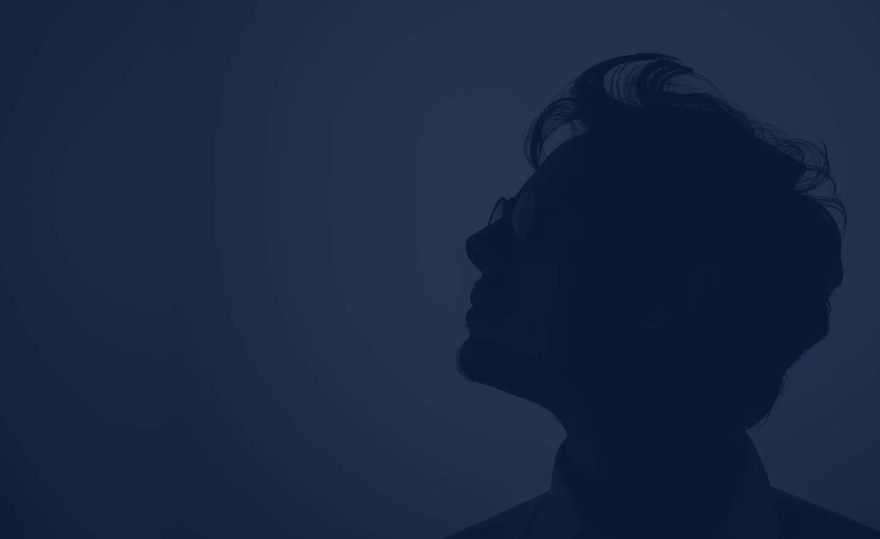 Silhouette of a man with glasses looking upward against a dark blue background.